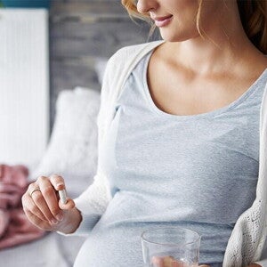 pregnant woman holding a capsule and a glass